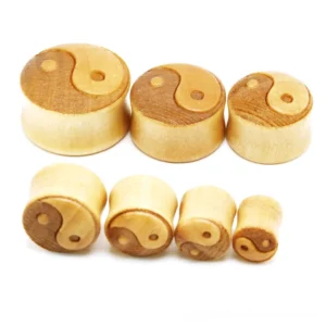 Close-up detail of bamboo ear tunnel expander showing intricate yin-yang carving and natural wood grain texture, golden tone finish