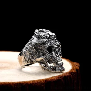 Adjustable biker skull ring side profile showing detailed dragon and skull carvings on antiqued silver, displayed on wooden vintage background