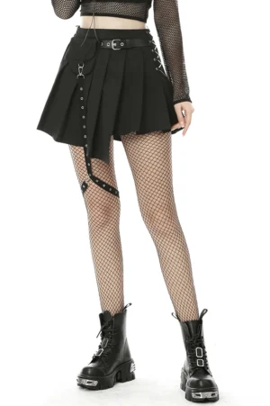 Black asymmetrical pleated gothic mini skirt with metal leg strap worn by model in front view, showcasing uneven hemline and rivet details