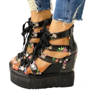 Black floral platform wedge gladiator sandals with lace-up front and buckle ankle straps, shown on model wearing ripped denim jeans