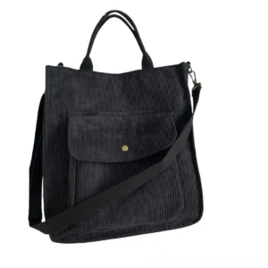 Black corduroy gothic tote bag with snap front pocket, flat lay view showcasing minimalist dark aesthetic and adjustable shoulder strap