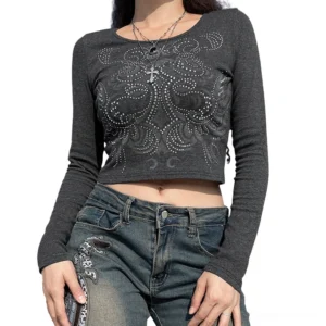 Women's black gothic crop top with rhinestone geometric pattern, long sleeves and crew neck, worn by model on street in casual dark outfit