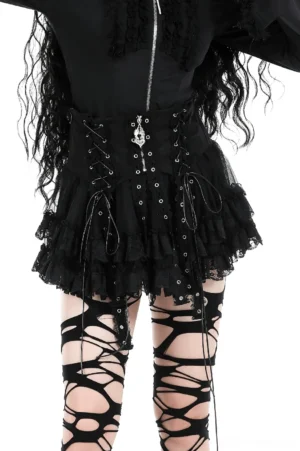 Black gothic mini skirt with lace corset waistband, cross zipper pendant, and ruffled tulle hem worn with matching lace top and fishnet stockings - front full view