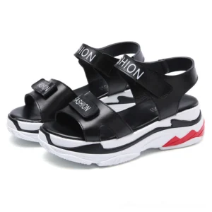 Black platform velcro sandals with red heel accents, front three-quarter view showing gothic-inspired design and bold lettering on adjustable straps