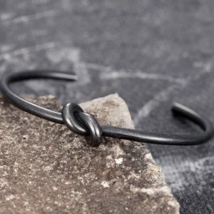Gothic knot open cuff bracelet flat lay overhead view on dark fabric and stone backdrop vintage black metal aesthetic