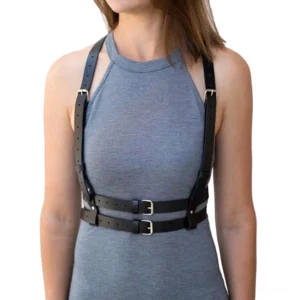 Black leather chest harness belt for women, front view showing dual adjustable waist straps with metal buckles, worn over gray halter dress, Gothic body harness