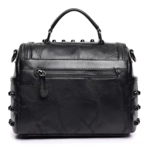 Rear view of black gothic leather crossbody bag featuring exterior zipper pocket and patchwork leather texture with all-over rivet embellishment