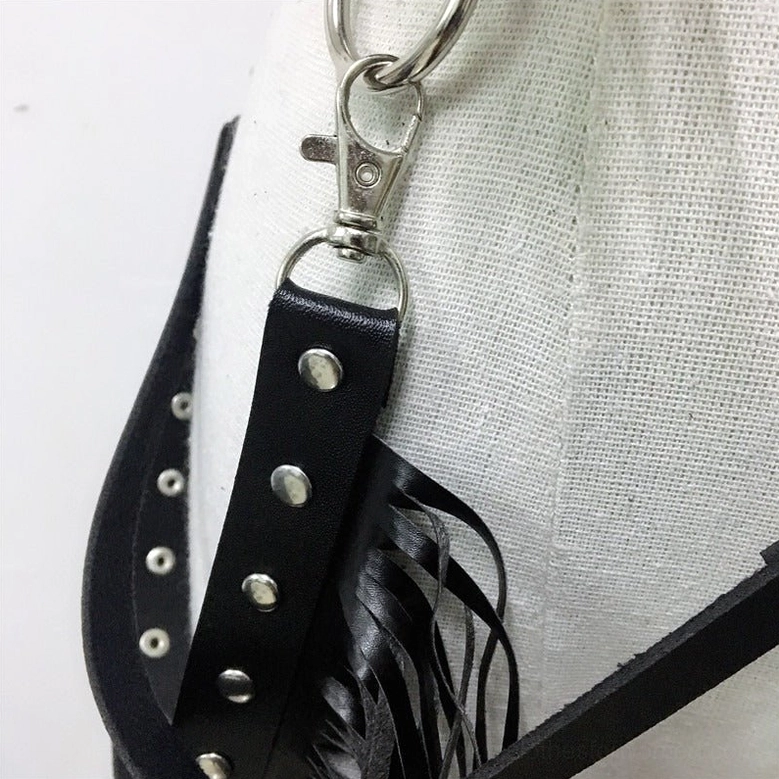 Macro close-up of gothic leather harness metal hardware including snap hooks, rivet fasteners, and stainless steel D-rings