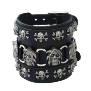 Black leather wide skull cuff bracelet with antique silver metal charms, front flat lay view showing adjustable buckle closure and skull ornaments