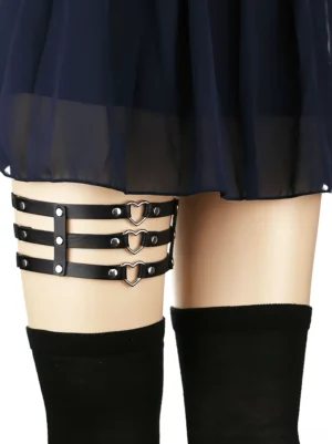 Black synthetic leather thigh harness with silver metal heart and rivet accents worn on model leg, side view