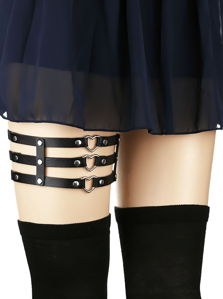 Black synthetic leather thigh harness with silver metal heart and rivet accents worn on model leg, side view