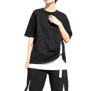 Black pleated gothic t-shirt with buttoned side strap and asymmetrical hem, front three-quarter view on model showing fake two-piece layered design