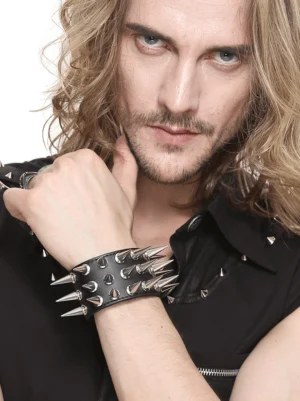 Wide black spiked cuff bracelet on long-haired male model, displaying adjustable snap fasteners and dense silver spike detail