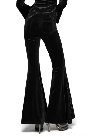 Rear three-quarter view of black velvet gothic pants displaying functional patch pockets and ruched high-waisted design from behind