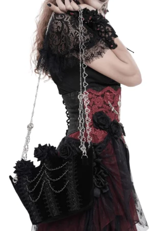 Black velvet gothic rose handbag worn on shoulder by model in gothic lace outfit, rear three-quarter view showing silver heart chain straps and embellished rose details
