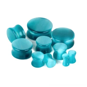 Overhead flat lay arrangement of blue cats eye stone ear plugs in multiple sizes showing double-flared gothic tunnel design and polished stone finish