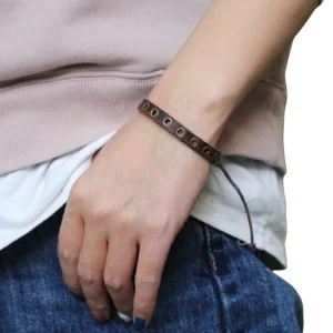 Brown leather grommet bracelet worn on female wrist, adjustable lace-up closure shown in lifestyle casual setting