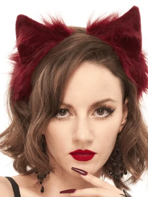 Front view of burgundy faux fur cat ears headpiece on model with short curly hair, hand pose near chin