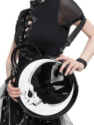 Female model wearing gothic black outfit styled with crescent moon skull round handbag, studio fashion photography