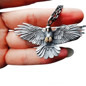 Detailed side close-up of silver crow pendant held on fingertips showing intricate feather texture and polished vintage finish