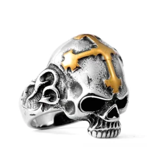 Gold stainless steel skull ring with ornamental cross on white background, front three-quarter view showing detailed carved skull face and band