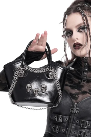 Model wearing black gothic tote bag with skull charms, styled with dark goth makeup and alternative fashion outfit