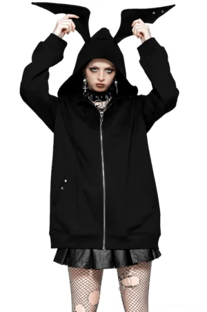 Black batwing zip hoodie with studded bat ear hood worn by female goth model in front view, paired with fishnet tights and dramatic dark makeup