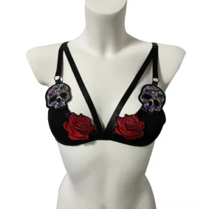Black gothic bralette with embroidered red roses and colorful sugar skull patches, front view with adjustable straps on white background