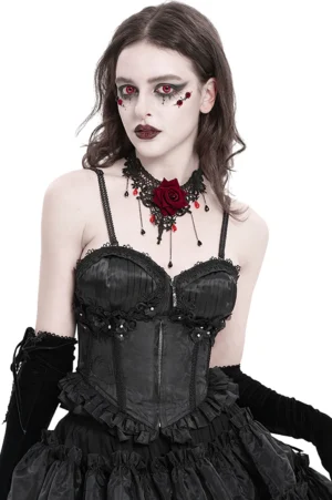 Black floral gothic corset with lace-up back worn by model with goth makeup, front three-quarter view showing zipper and ruffle hem detail