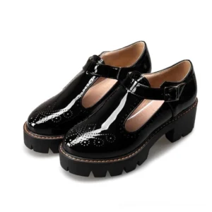 Black patent leather gothic brogue platform flats with T-strap buckle, shown from three-quarter side view displaying intricate brogue perforations