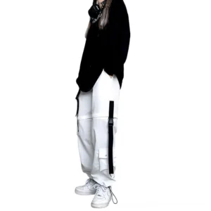 White and black color block gothic cargo pants with strap embellishments shown from side angle, demonstrating tapered ankle cuff and high-waist design