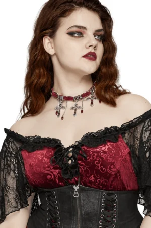 Red velvet choker with ornate cross pendants on model wearing gothic corset dress with sheer lace sleeves, side-front angle