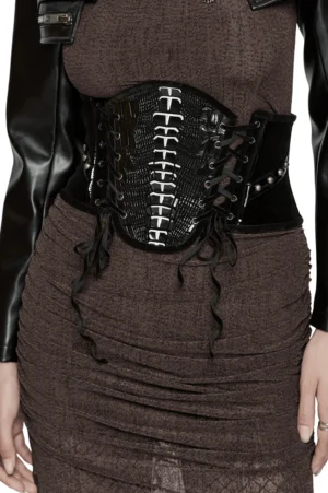 Gothic corset belt with spinal rivets and black velvet front panel worn by model, front half-body view showing structured waistline and patent leather accents