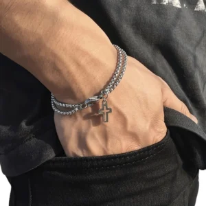 Double chain cross pendant bracelet worn on male left wrist close-up side view showing silver metal finish and chain texture in casual daily wear