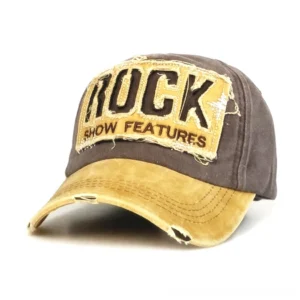 Distressed gothic baseball cap with ROCK SHOW FEATURES embroidery in brown and yellow, front 3/4 view showing frayed brim and two-tone distressed cotton fabric