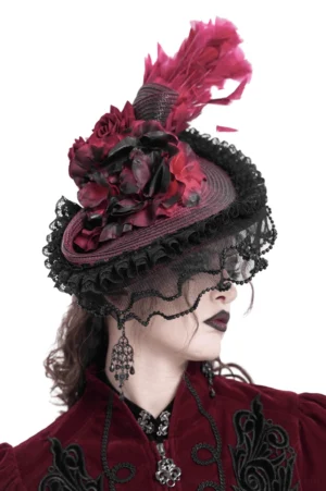 Alternative fashion model left side profile wearing burgundy black fascinator with matched velvet coat and dangling gothic earrings, detailed lace trim visible