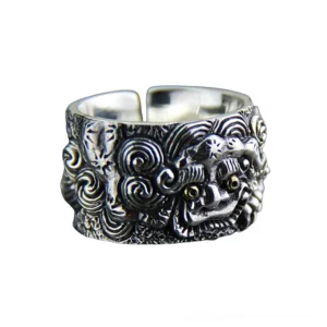 Adjustable gothic foo dog sterling silver ring frontal view, showing intricate mythical beast carving with aged silver patina and gold-toned eyes on white background