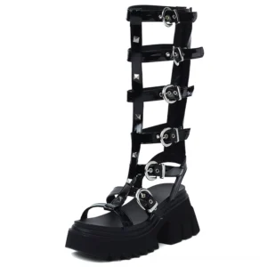 Black glossy leather knee-high gladiator platform sandals with silver pyramid studs and buckle straps, front left view studio photography