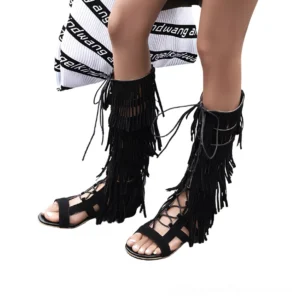 Black gothic gladiator sandals worn by female model, low angle frontal view showcasing cross foot straps and tiered tassels