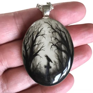 Close-up of glossy resin gothic graveyard pendant with silver metal frame held in hand showing texture and artistic detail of hand-painted cemetery scene