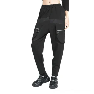 Black gothic harem cargo pants front three-quarter view showing elastic waist and fake zipper pockets on female model
