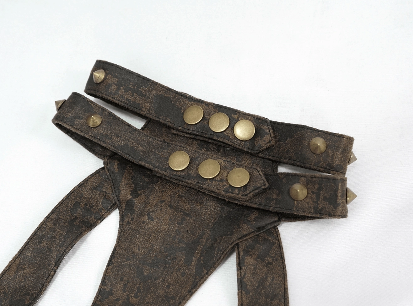 Close-up flat lay of gothic harness leather straps with dark brown distressed texture and bronze stud rivets