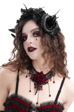 Gothic spiral horn headpiece with black floral feather accents and ribbon ties, worn by model with curly brown hair in left profile view