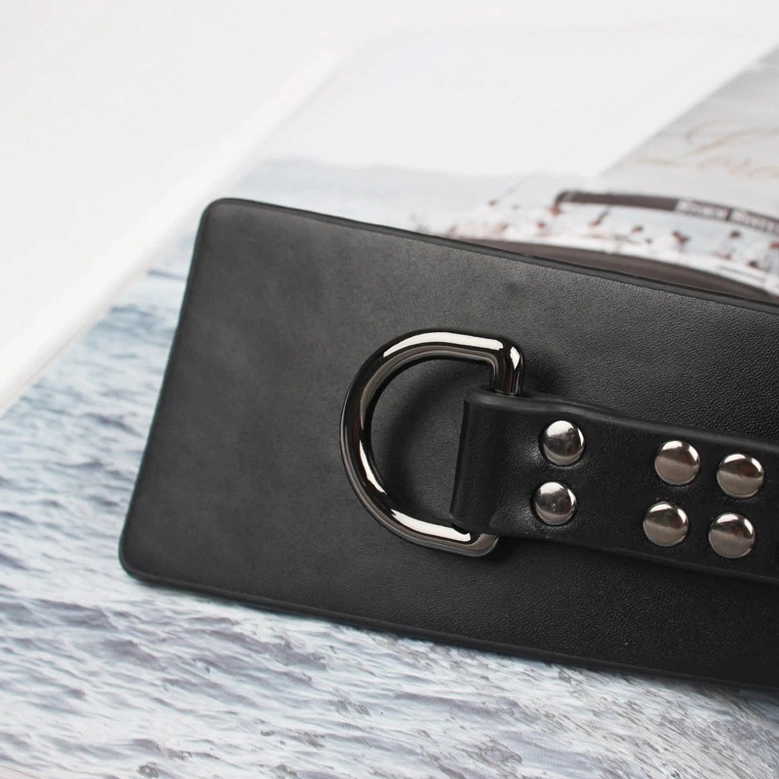 Close-up flat lay of black wide leather corset belt with D-ring buckle and multiple silver rivets on lifestyle background