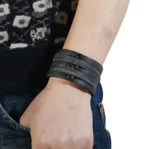 Black leather gothic bracelet worn on male wrist with denim outfit, adjustable snap closure detail visible