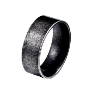 Minimalist stainless steel gothic ring displayed from three-quarter angle, showcasing weathered matte black metal finish and smooth band design on white background