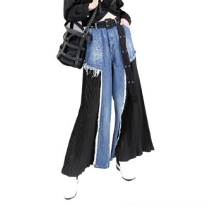 Gothic patchwork high-waist wide-leg denim trousers worn by model, front three-quarter view showcasing indigo blue denim with black pleated side panels and frayed edges