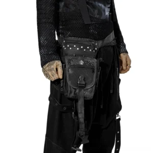 Punk apocalypse gothic waist bag front three-quarter view with rivets and skull badges, worn by male model with tattoos against white studio background