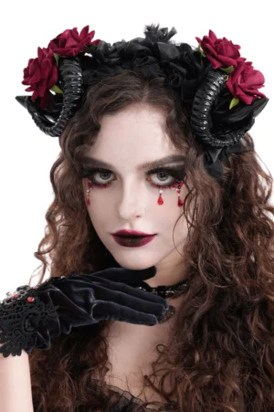 Gothic ram horn headpiece with crimson velvet roses worn by model with curly brown hair, front portrait view showcasing dramatic goth makeup and black fabric base