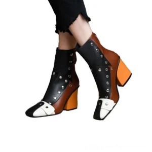 Woman wearing gothic riveted leather ankle boots with color-blocking and square heel, paired with black cropped trousers